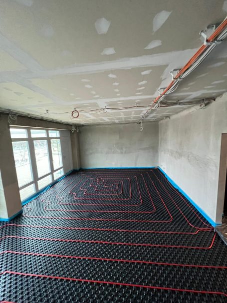 Boden mit schwarzem Heizsystem und roten Leitungen in leerem Raum.