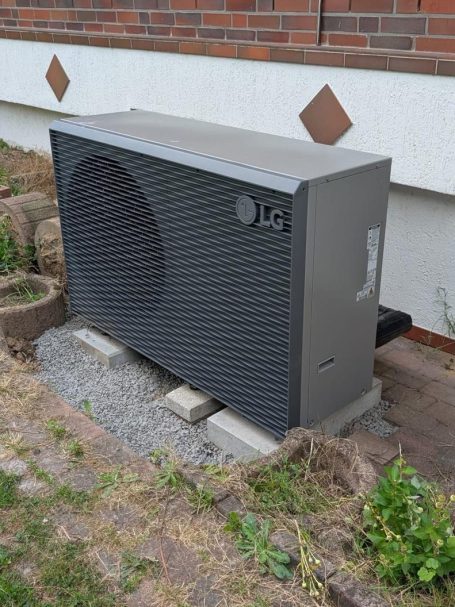 Graue Klimaanlage steht auf einem Betonfundament neben einem Gebäude.