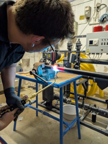 Handwerker verwendet eine Lötlampe an einem Tisch, um Metall zu bearbeiten.