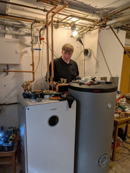 Mann arbeitet an Heizungs- und Warmwasseranlagen in einem technischen Raum.